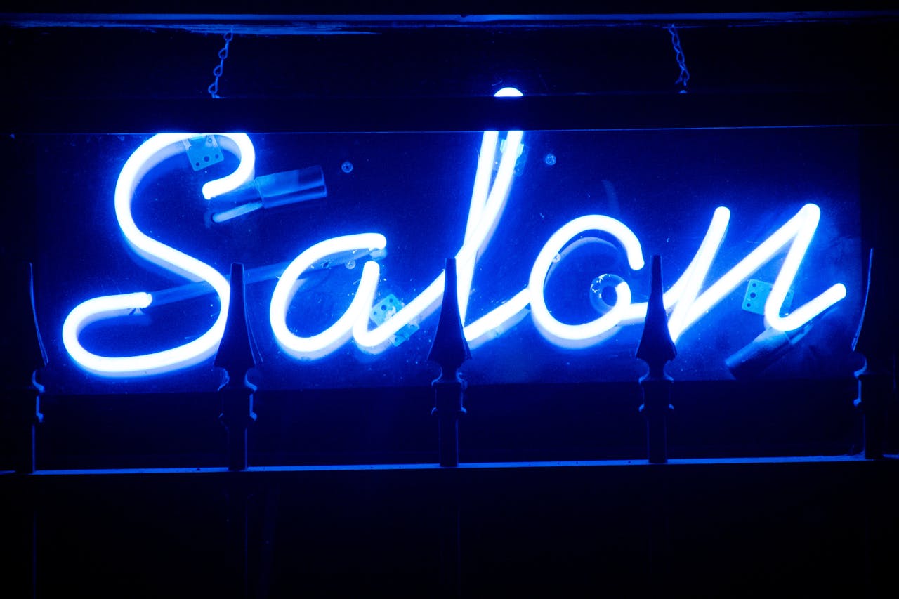 who-we-are Vivid blue neon salon sign glowing brightly in the dark.