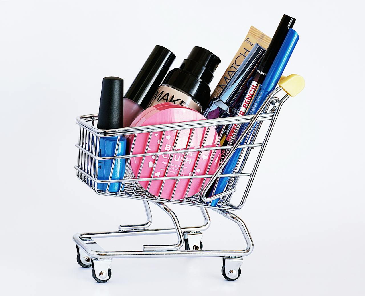 services-05 Miniature shopping cart filled with a variety of cosmetics on a white background.