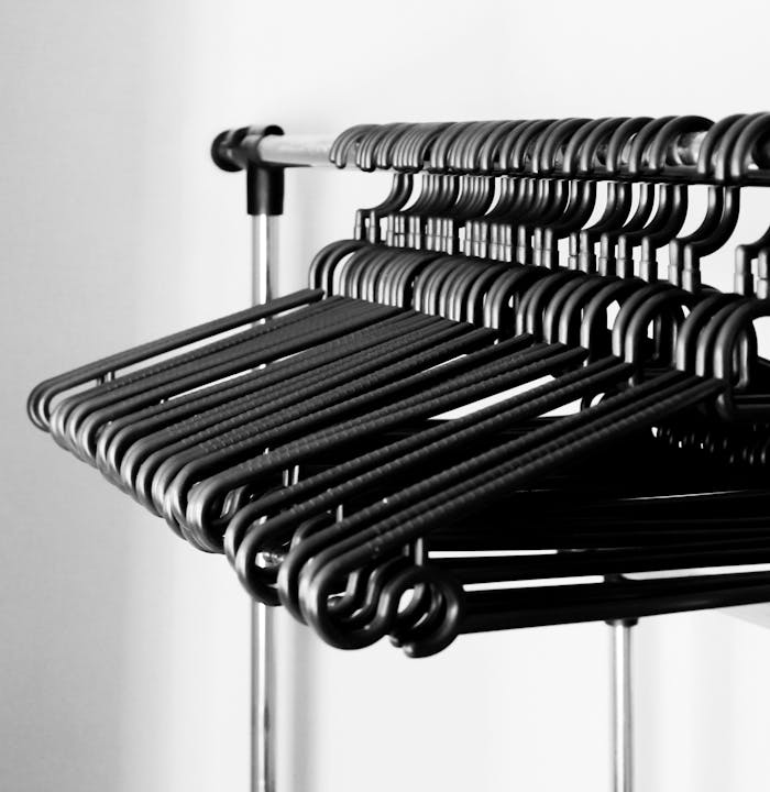 A modern grayscale image of clothes hangers neatly arranged on a metal rack indoors.